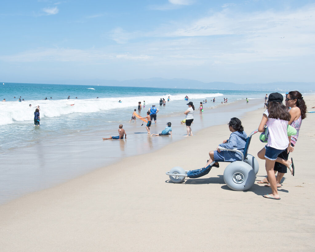 Someone using a beach wheelchair at Dockweiler Beach looks at the ocean